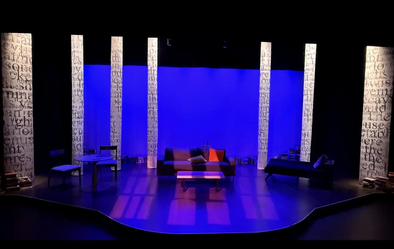 The Kaplan Family Stage lit in blue, with text-covered columns framing a living-room set